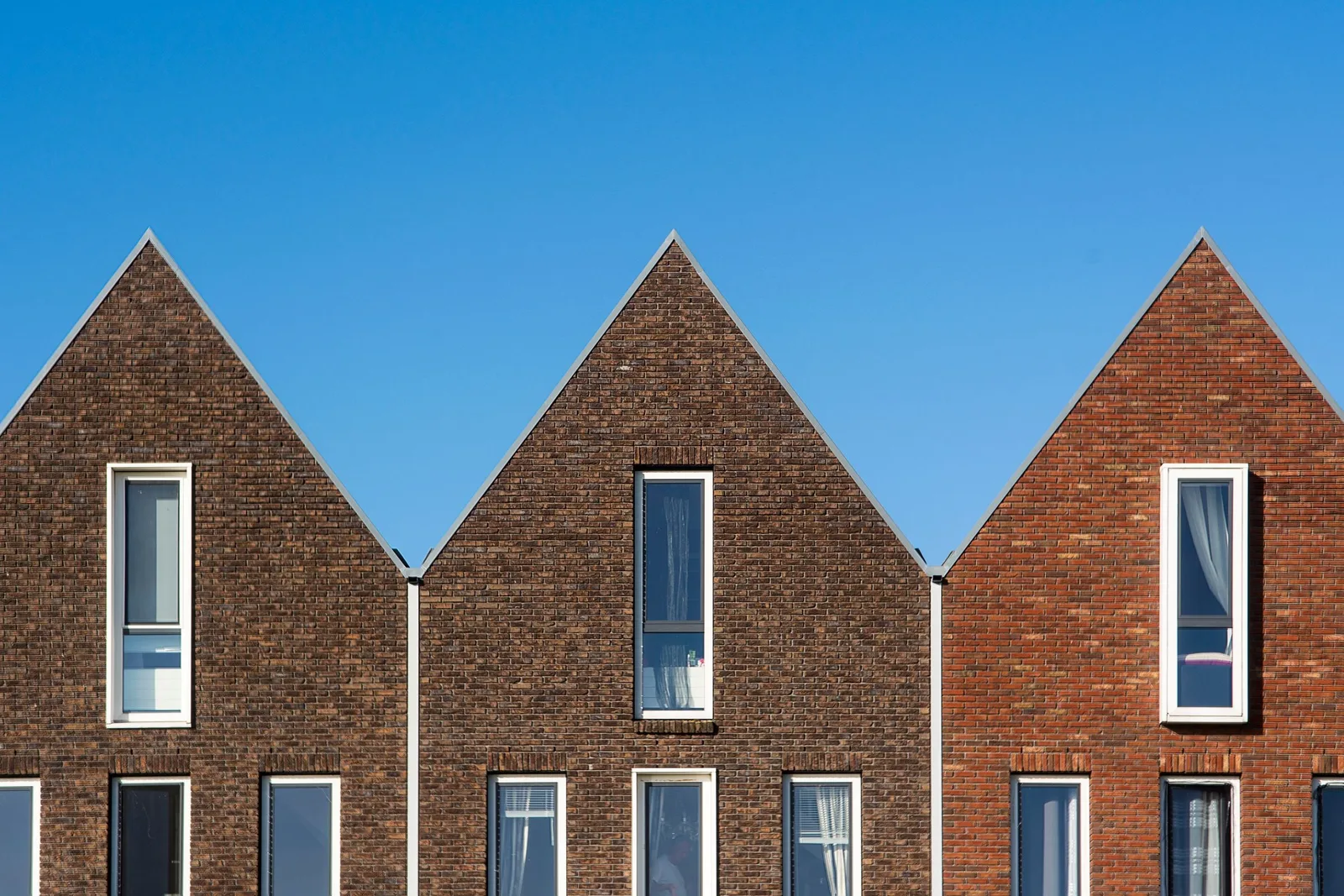 Three new brick houses with steep gabled roofs and tall narrow windows against a clear blue sky